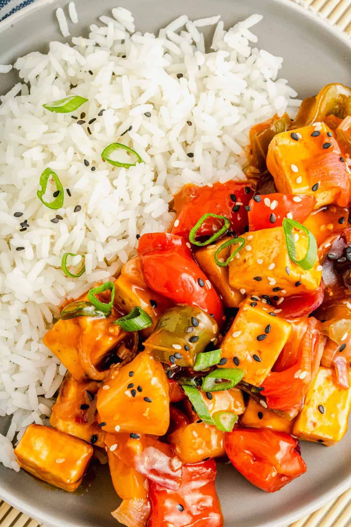 Sweet and sour tofu is plated next to a fluffy serving of white rice.