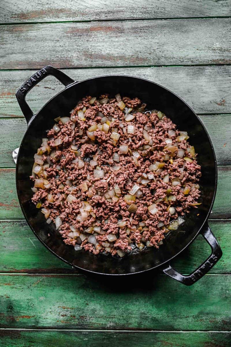 ground beef and onions are cooking together in a skillet.