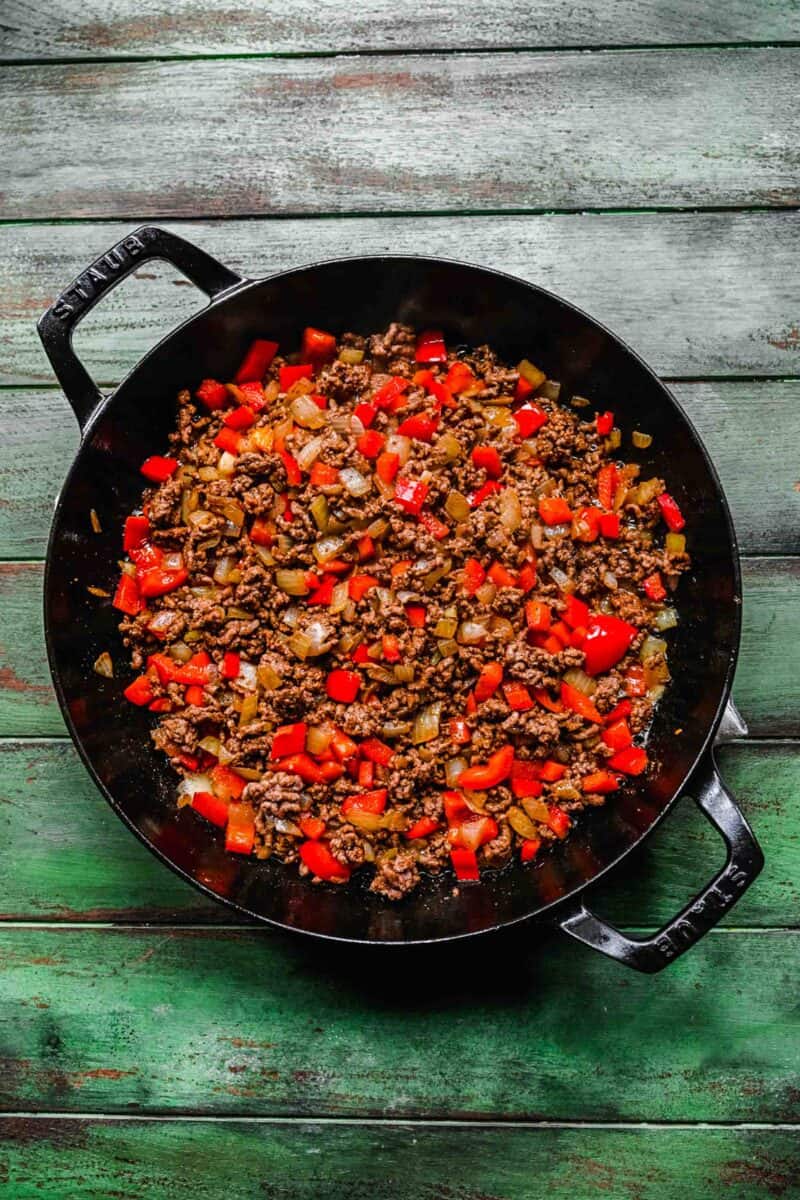 vibrant red bell peppers and ground beef are cooking together in a skillet.