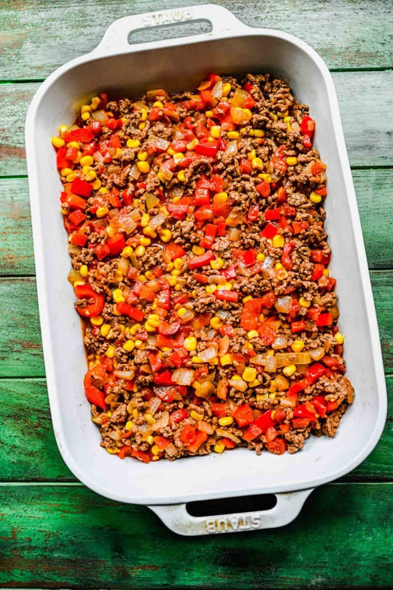 veggies and ground beef are spread in an even layer in a casserole dish.