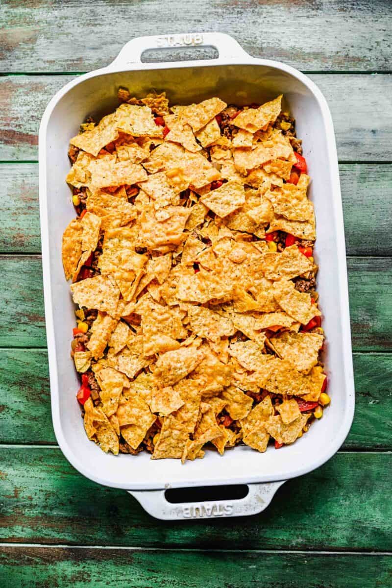 tortilla chips are cracked into smaller pieces and layered in a casserole dish.