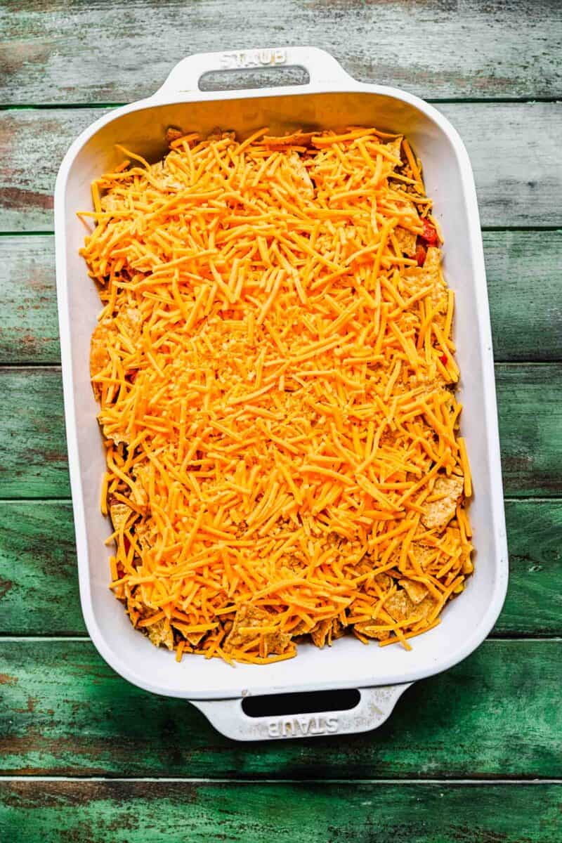 a layer of shredded cheese is presented in a white casserole dish.