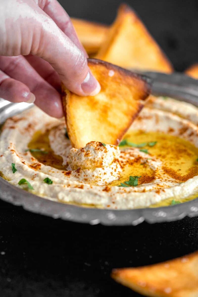 a pita chip is being dipped into a bowl filled with Baba Ganoush.