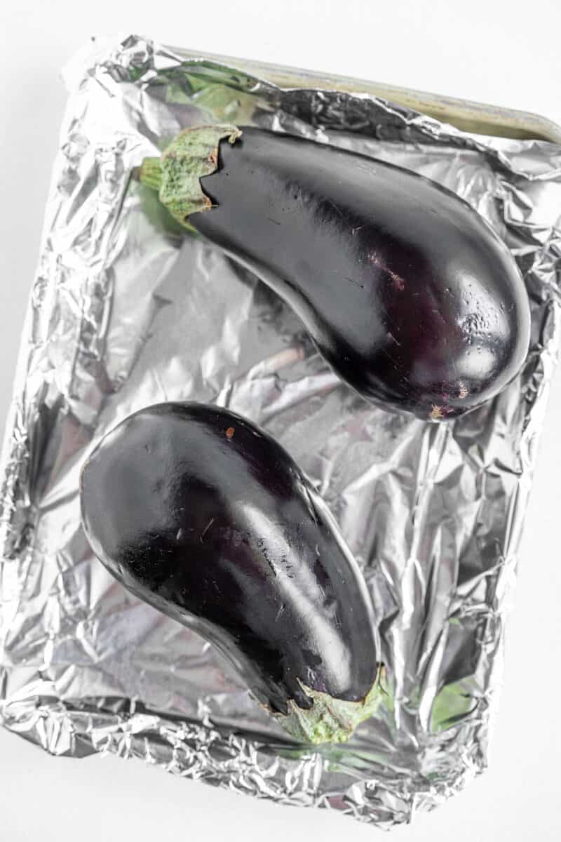 two raw eggplants are placed side by side on a baking sheet.