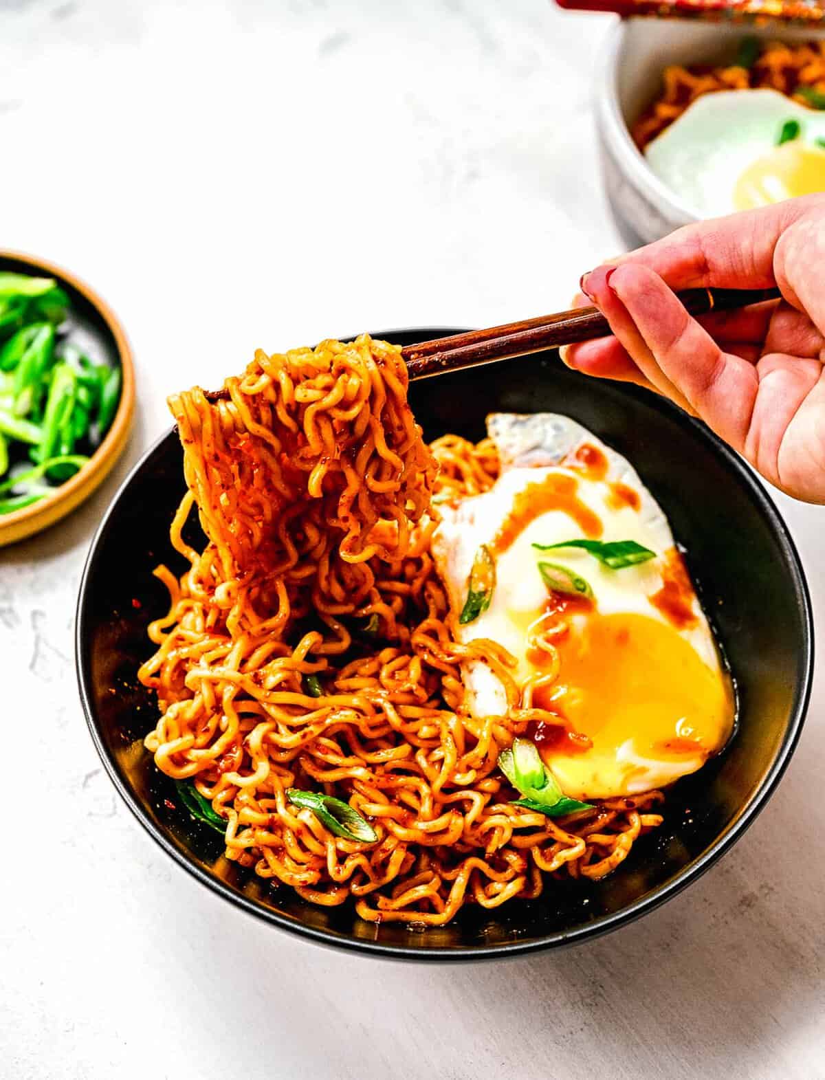 Instant ramen noodles are coated in a full-flavored, spicy sauce in this delicious, quick, and easy buldak ramen recipe. Chopsticks taking a bight of buldak ramen noodles.