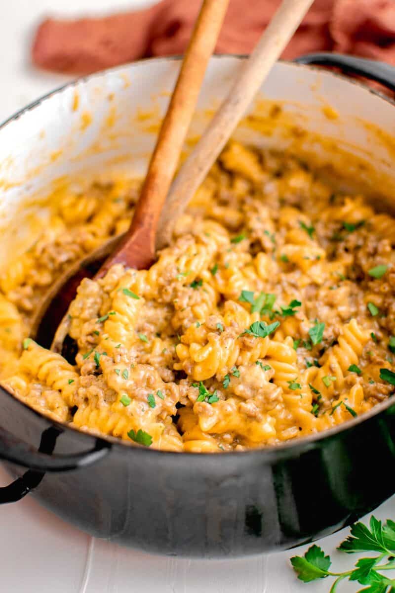 cheeseburger pasta is being mixed in a pot with two wooden spoons.