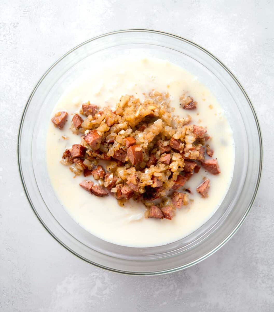 sausage and onion mixture added to a large clear bowl with egg mixture and shredded potatoes