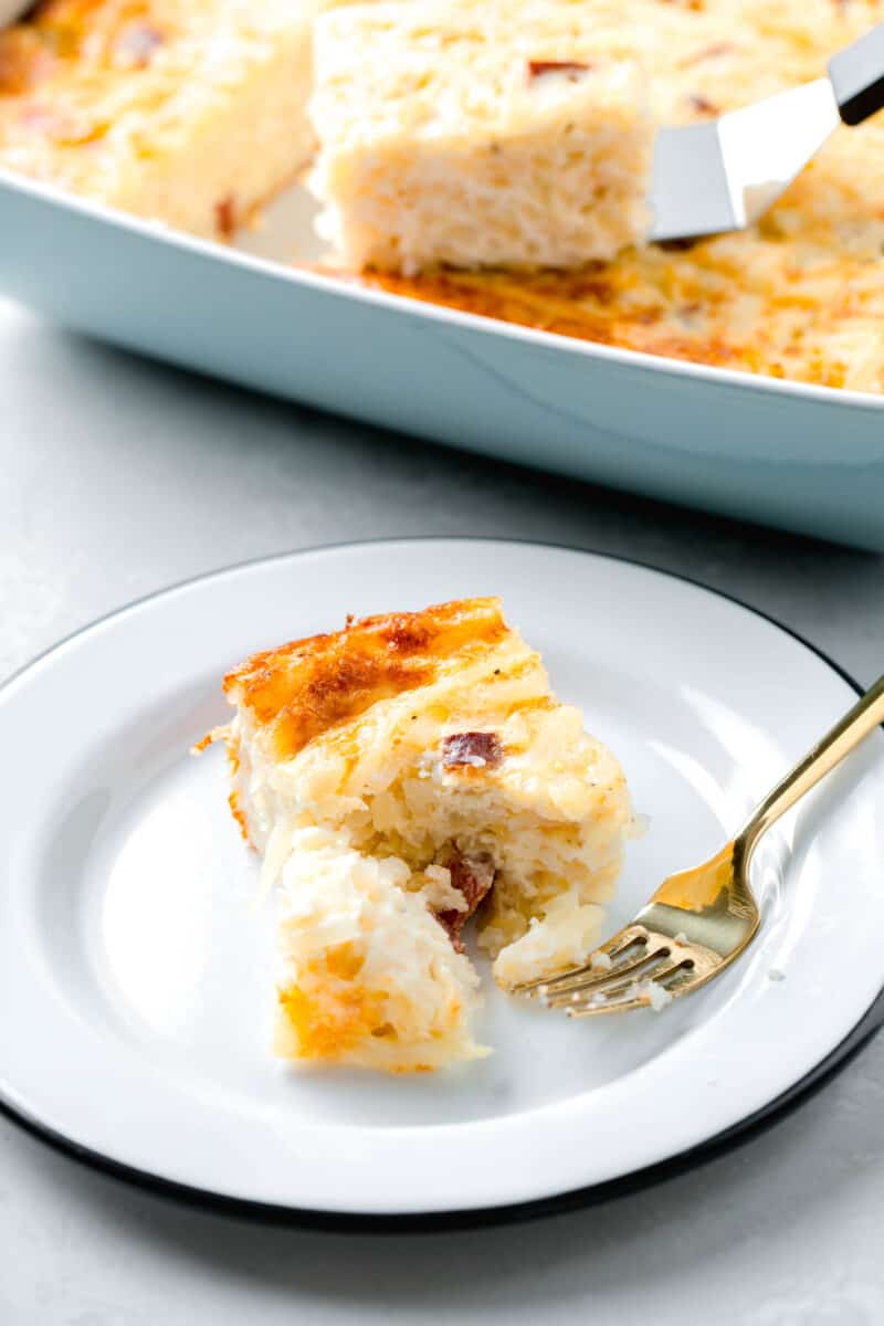 a slice of egg white breakfast casserole on a white black rimmed plate with a gold fork and a piece of the casserole cut off