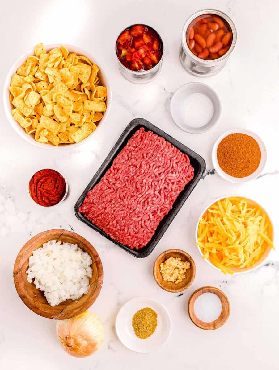 the ingredients for frito chili pie are presented on a white surface.