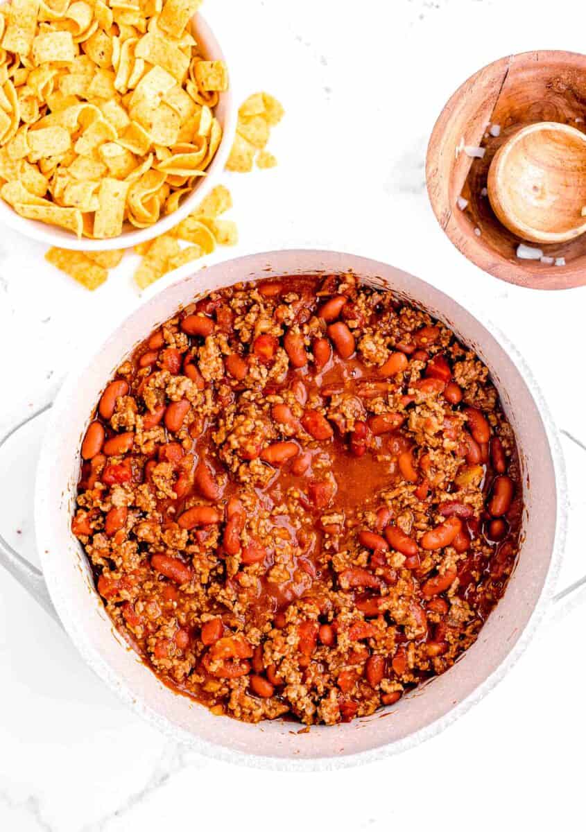 cooked chili is presented on a white surface next to a small white bowl filled with frots.