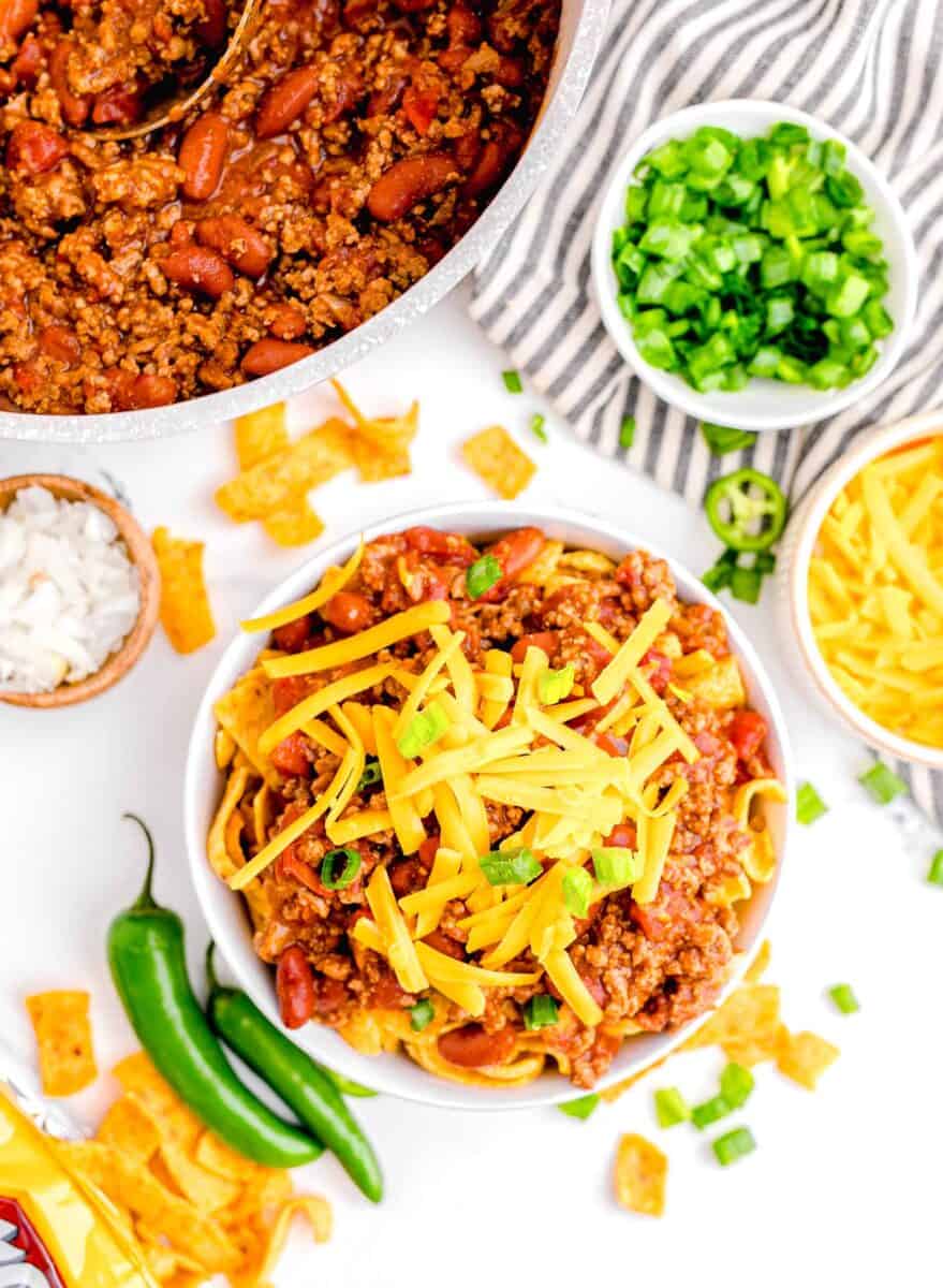shredded cheddar cheese and green onions are used as garnishes on top of a bowl of chili.