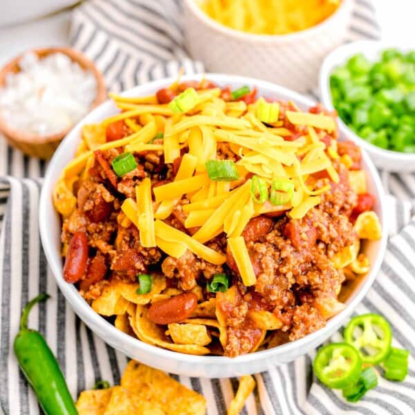 a garnished bowl of frito chili pie is placed on a striped tea towel.