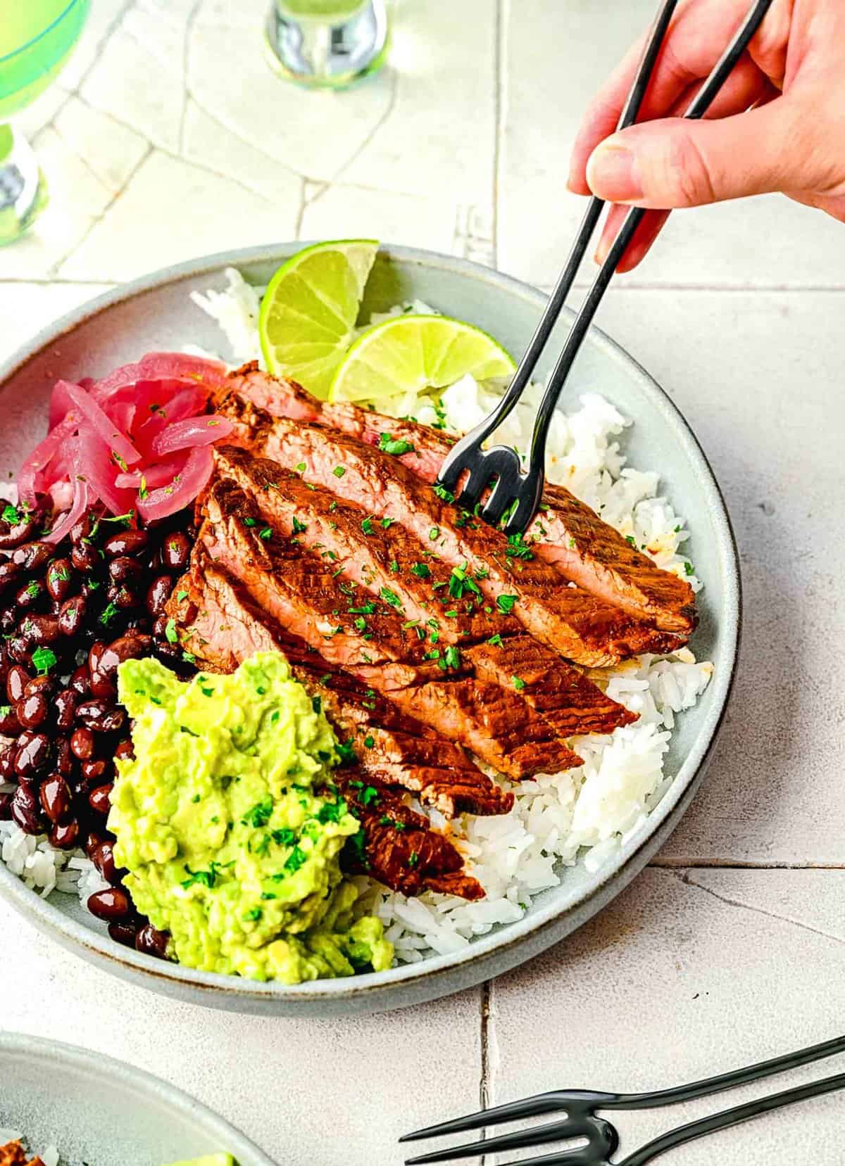 Garlic guajillo steak in a burrito bowl with a fork digging in.