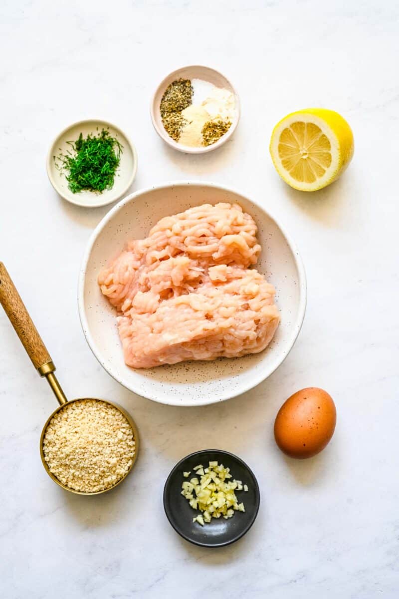 the ingredients for greek chicken meatballs are placed on a white surface.