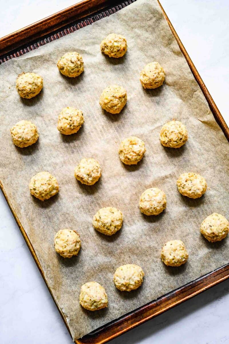 meatballs have been rolled out and placed on a sheet of parchment paper on a baking sheet.