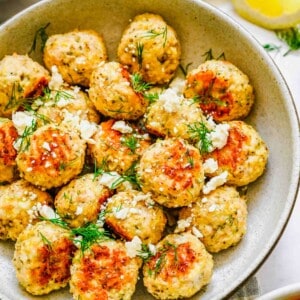 meatballs in a bowl are garnished with cheese and herbs.