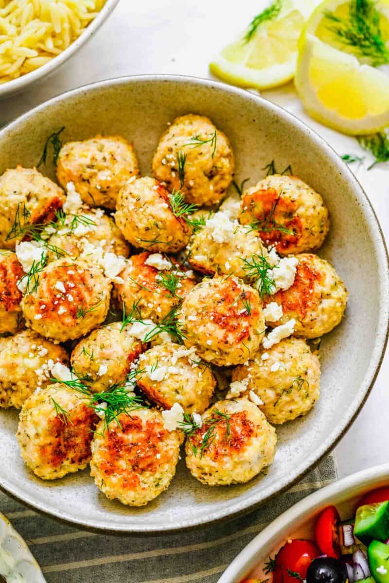 meatballs in a bowl are garnished with cheese and herbs.
