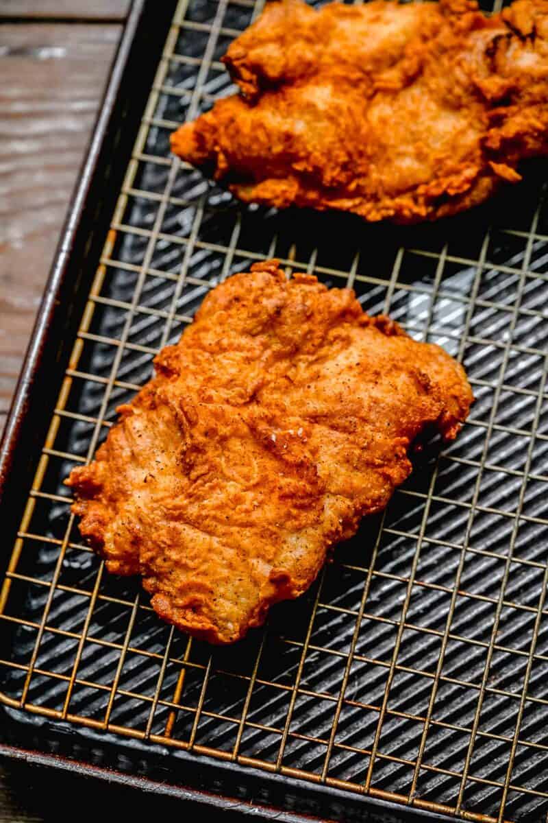 Draining excess oil from fried chicken on a wire rack over a baking sheet.