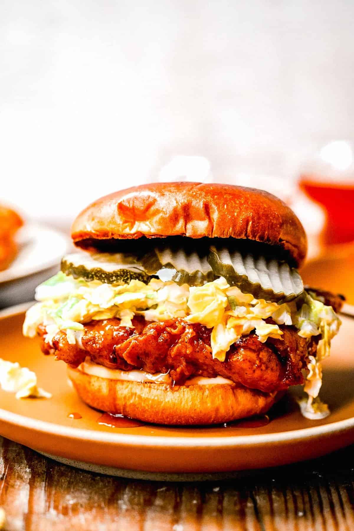 Crunchy fried chicken smothered in spicy honey is sandwiched between brioche buns and cooled down just the right amount by a refreshing slaw. Hot honey chicken sandwhich on a plate.
