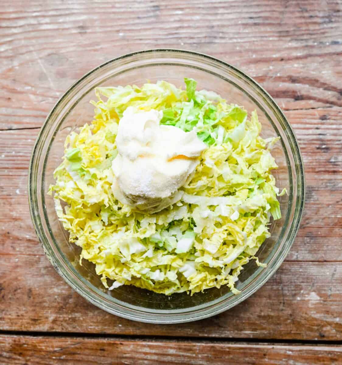 Cabbage in a bowl with mayonnaise, white vinegar, granulated sugar, and kosher salt.