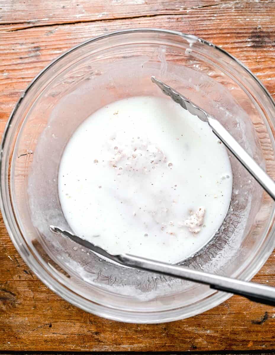 Dipping dredged chicken in buttermilk with tongs.