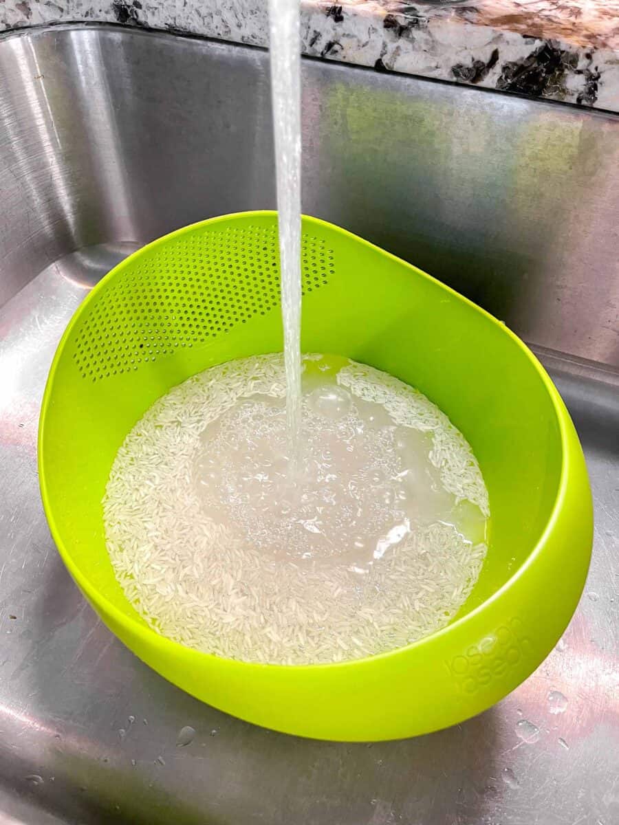 water running into bright green colander with uncooked jasmine rice