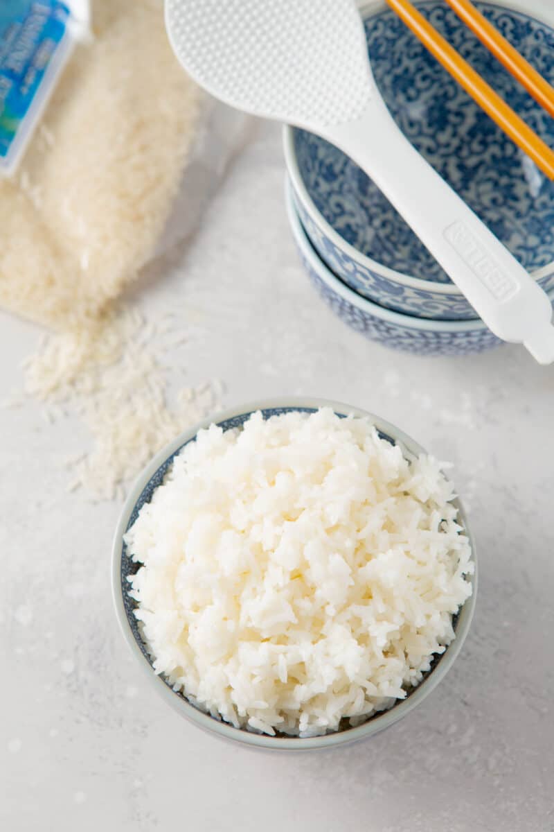 overhead image of instant pot jasmine rice next to a rice paddle and uncooked rice