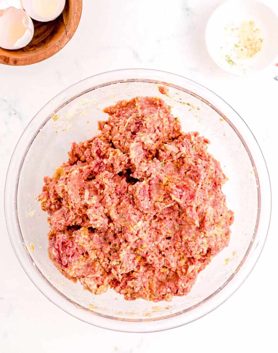 the ingredients for meatloaf have been combined in a glass bowl to form a mixture.