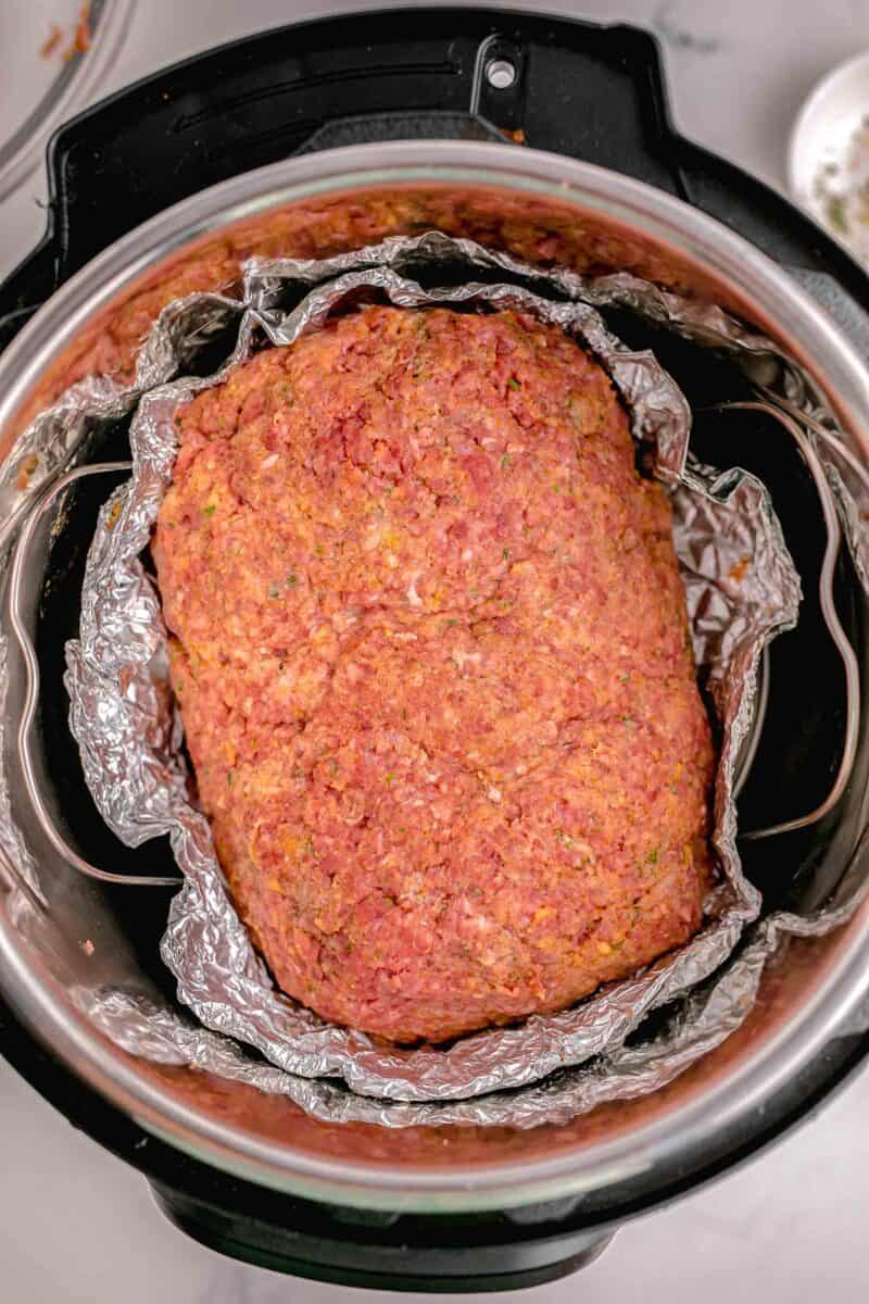 an uncooked meatloaf is in a foil loaf pan in the instant pot.