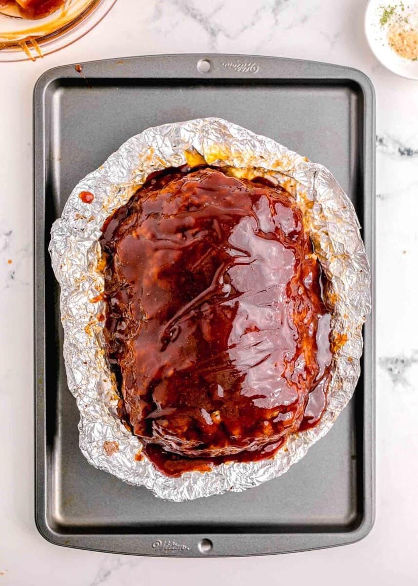 a glazed meatloaf is placed in foil on a baking sheet.