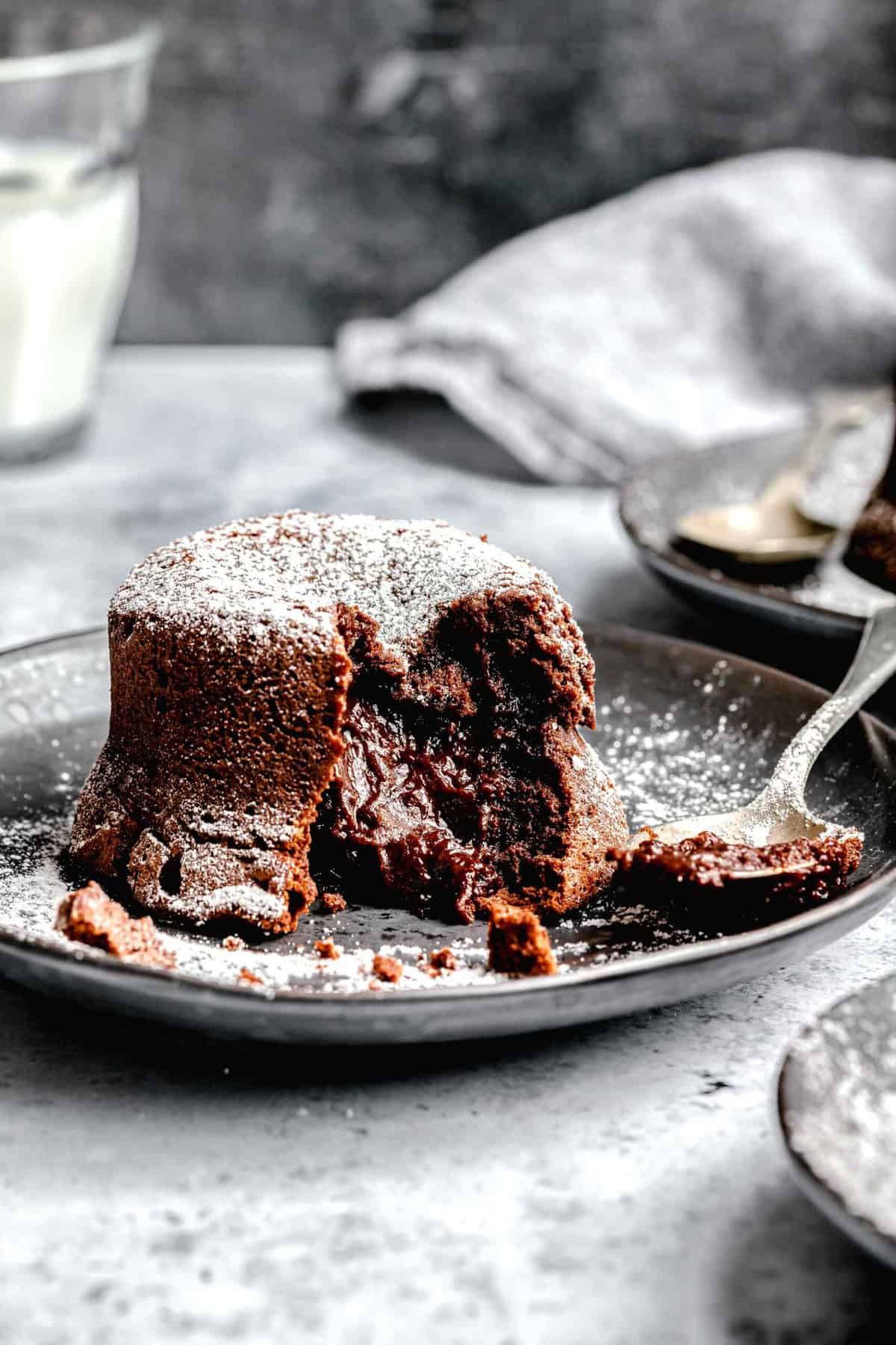 Molten lava cake served on a plates with a spoon near a glass of milk.