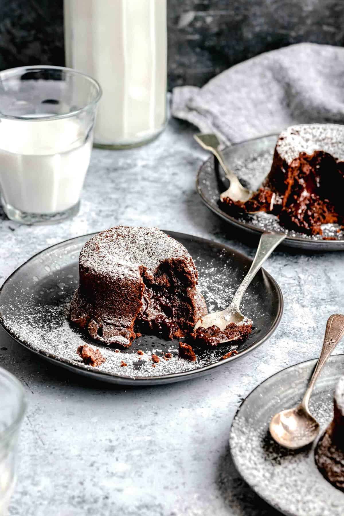 Molten lava cake served on plates with spoons near a glass of milk.