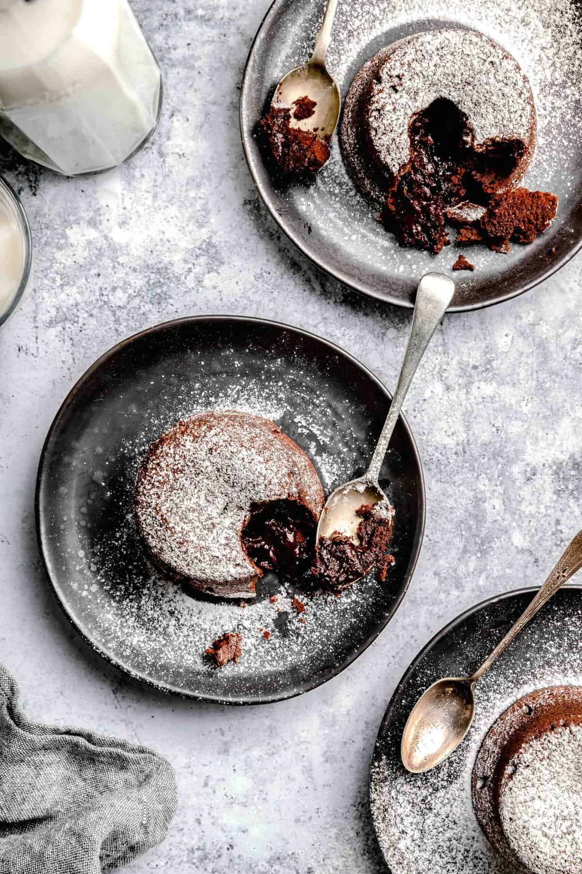 Molten lava cake served on plates with spoons near a glass of milk.