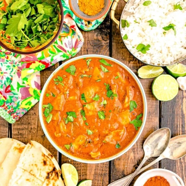 rice, cilantro and limes are placed around a bowl filled with butter chicken.