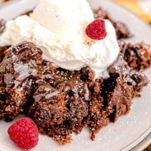 a close up image shows whipped cream and raspberries on top of a cake.