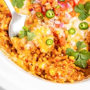 a large serving spoon is dipping into enchilada casserole.