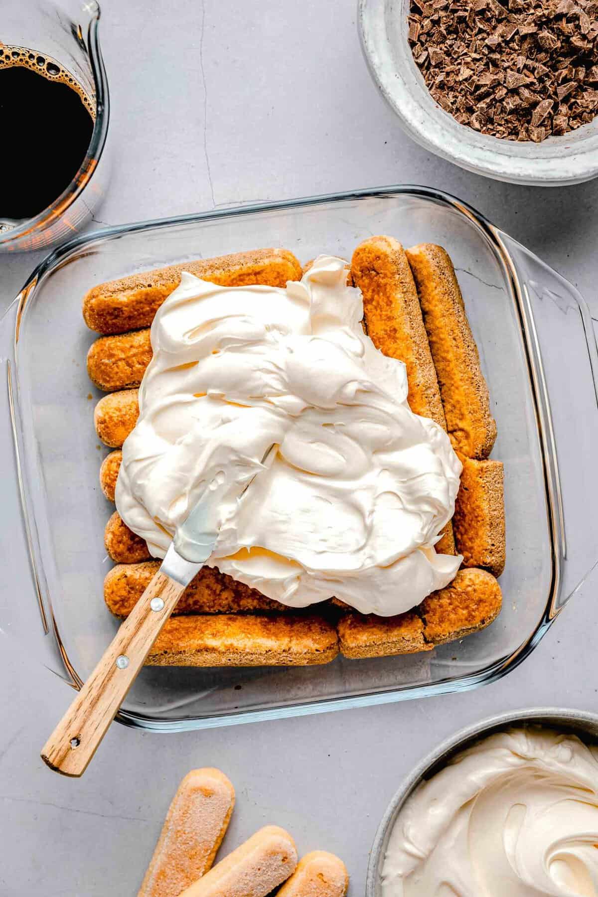 Spreading mascarpone filling over espresso soak lady fingers in a baking pan.