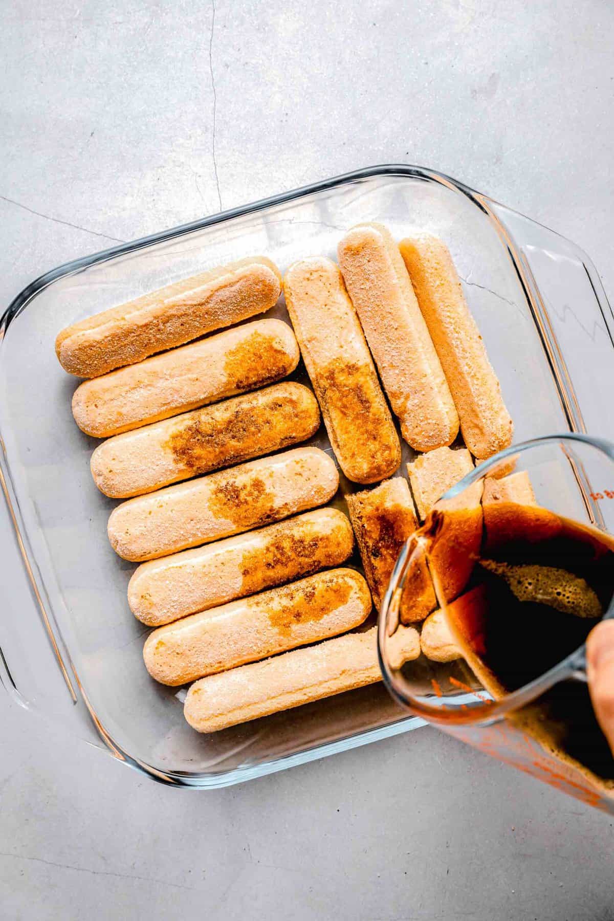 Pouring espresso over ladyfingers in a baking gpan.