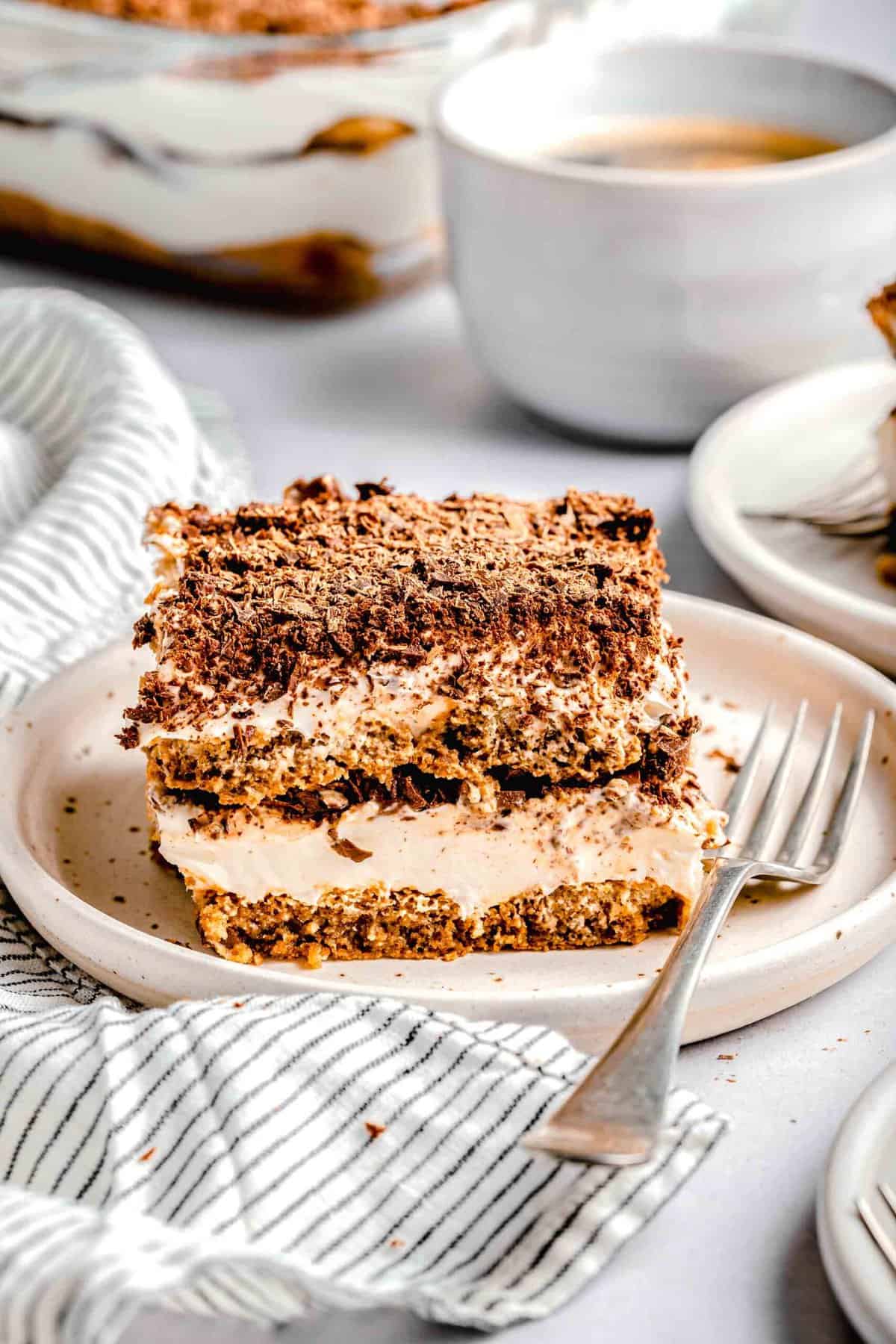 A slice of tiramisu on a plate with a fork near a cup of espresso.