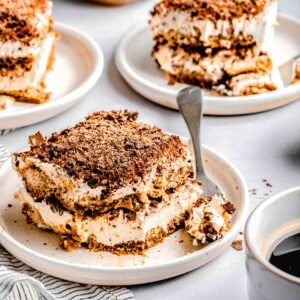 Slices of tiramisu on plates with forks near a cup of espresso.