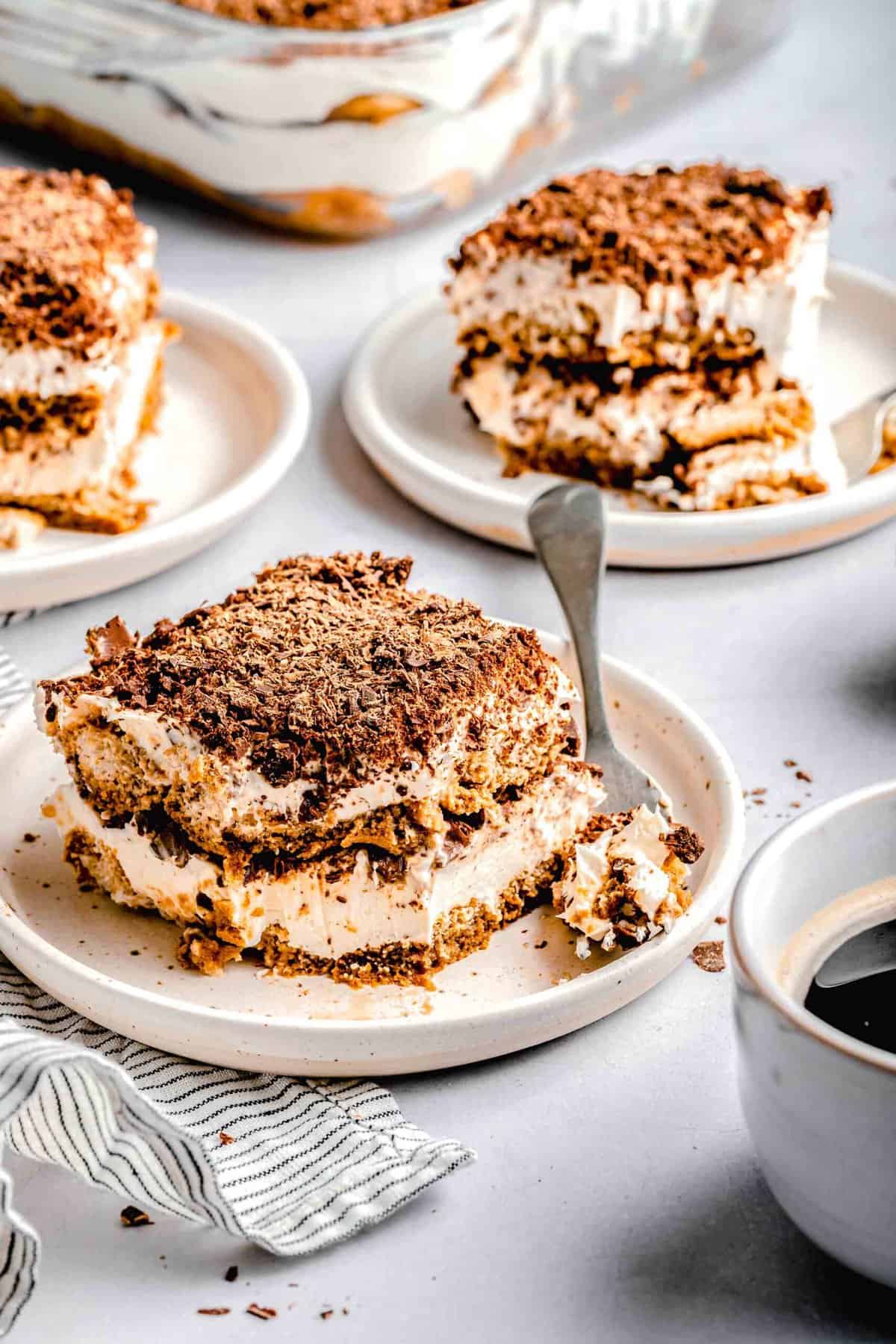 Slices of tiramisu on plates with forks near a cup of espresso.