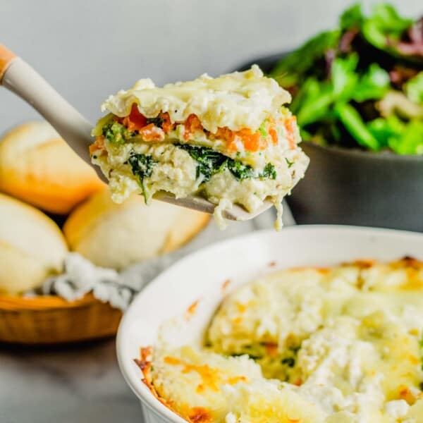 a slice of white lasagna is being lifted from the baking dish.