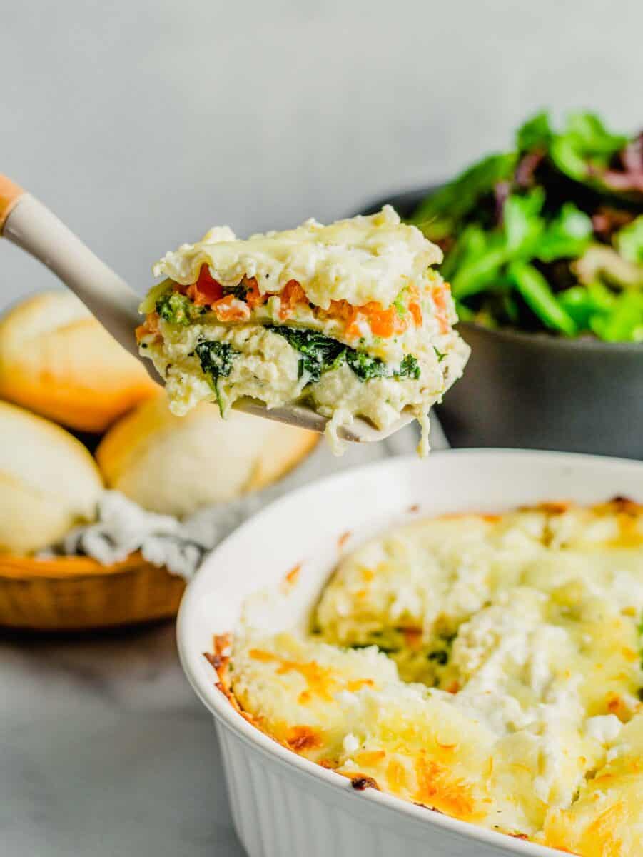 a slice of white lasagna is being lifted from the baking dish.