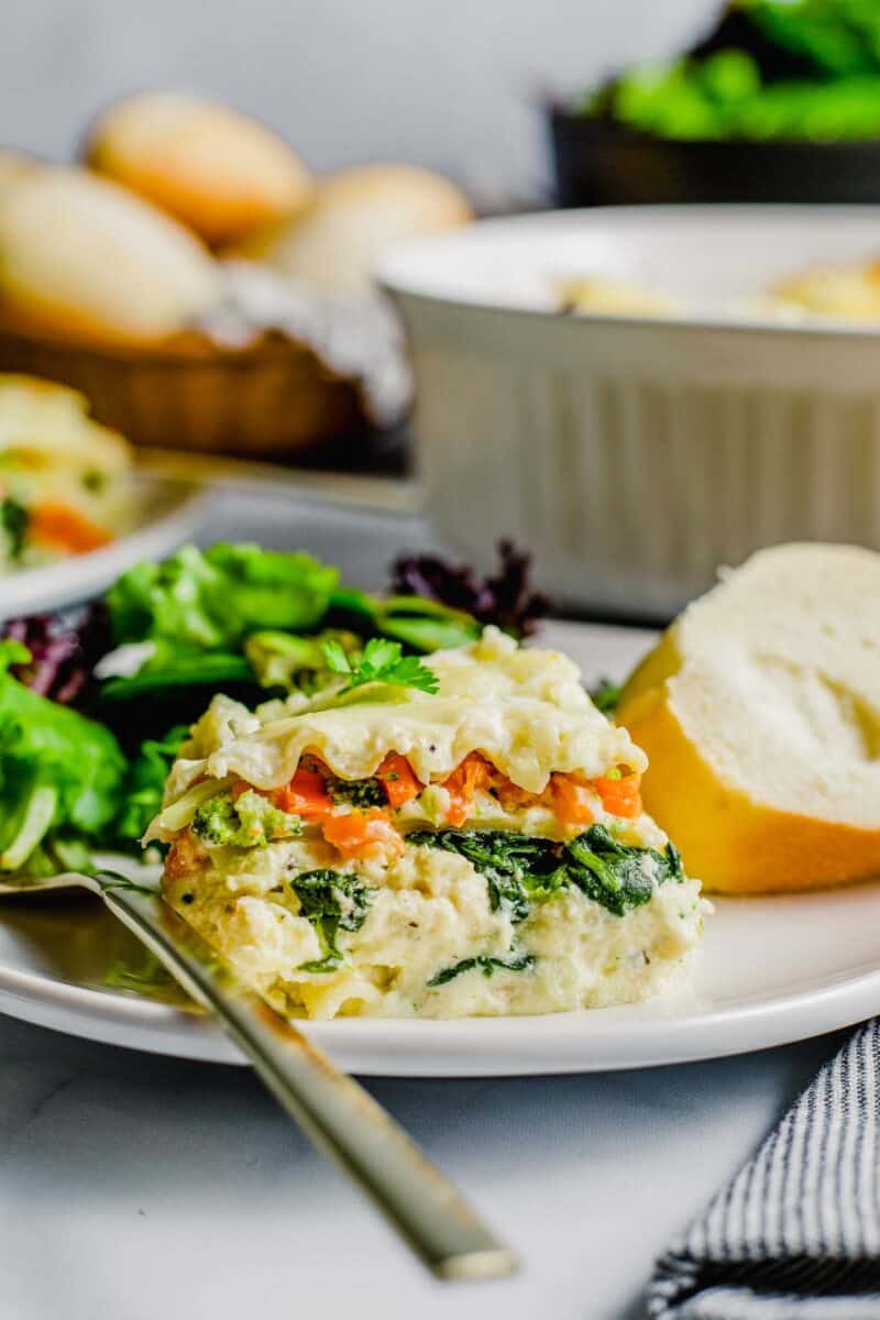 a serving of lasagna is placed next to bread and a side salad.