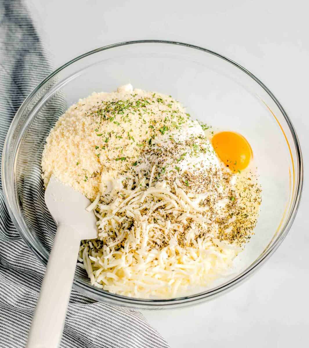 cheese, egg, and seasonings are placed in a glass mixing bowl.