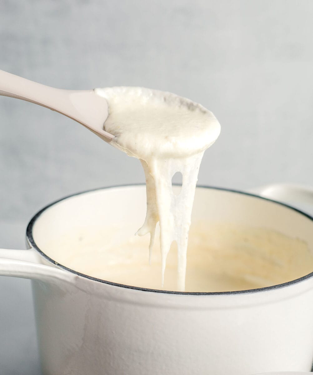 a spoon is mixing creamy white cheese sauce.
