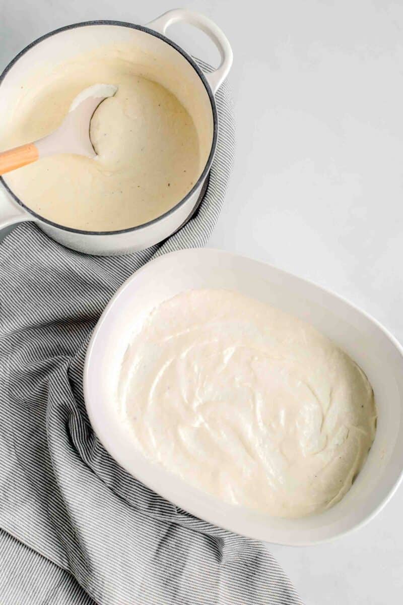 white sauce is smoothed on the bottom of a white casserole dish.