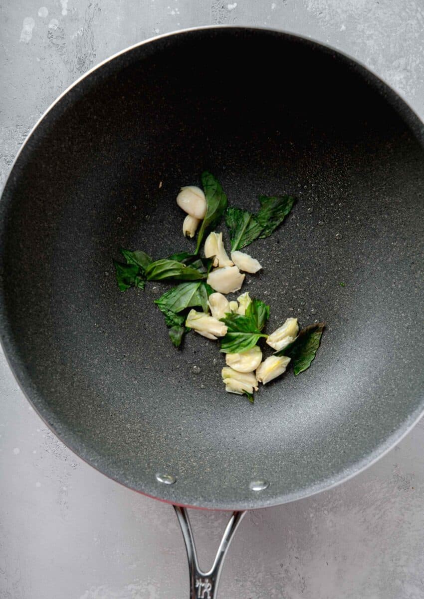 smashed garlic and thai basil in a grey nonstick skillet