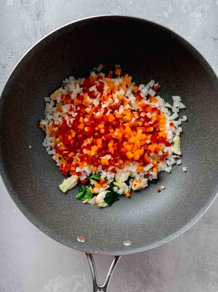 red and orange diced bell peppers and diced onions added to the nonstick skillet with the garlic and thai basil