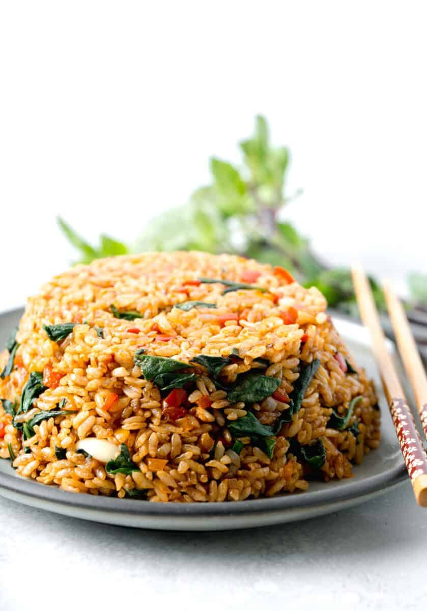 thai basil fried rice in a bowl mold on top of a grey ceramic plate with wooden chopsticks
